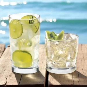 Set de 12 vasos de vidrio Cristar Madeira con bebidas, ambientados junto al mar sobre una mesa de madera