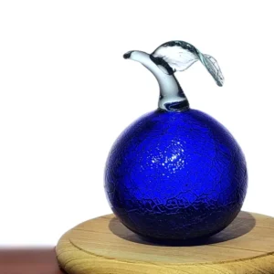 Adorno de manzana en vidrio azul cobalto con textura craquelada, exhibido sobre una base de madera redonda.