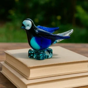 igura de paloma de vidrio azul artesanal usada como adorno o pisapapeles sobre una pila de libros en un jardín.