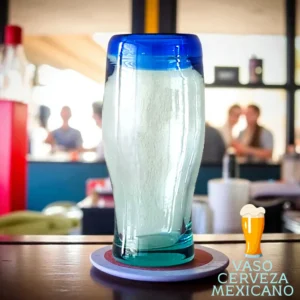 Vaso cervecero mexicano de vidrio soplado con borde azul sobre mesa de madera