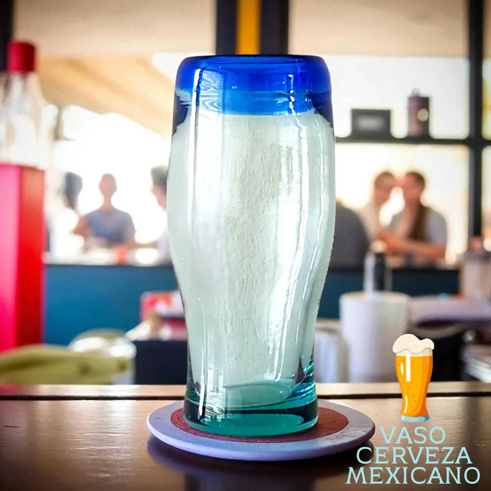 Vaso cervecero mexicano de vidrio soplado con borde azul sobre mesa de madera
