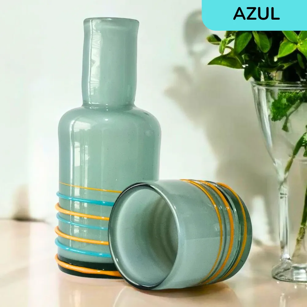 Botella de vidrio azul artesanal con vaso a juego y detalles en hilo, mostrando su diseño decorativo.