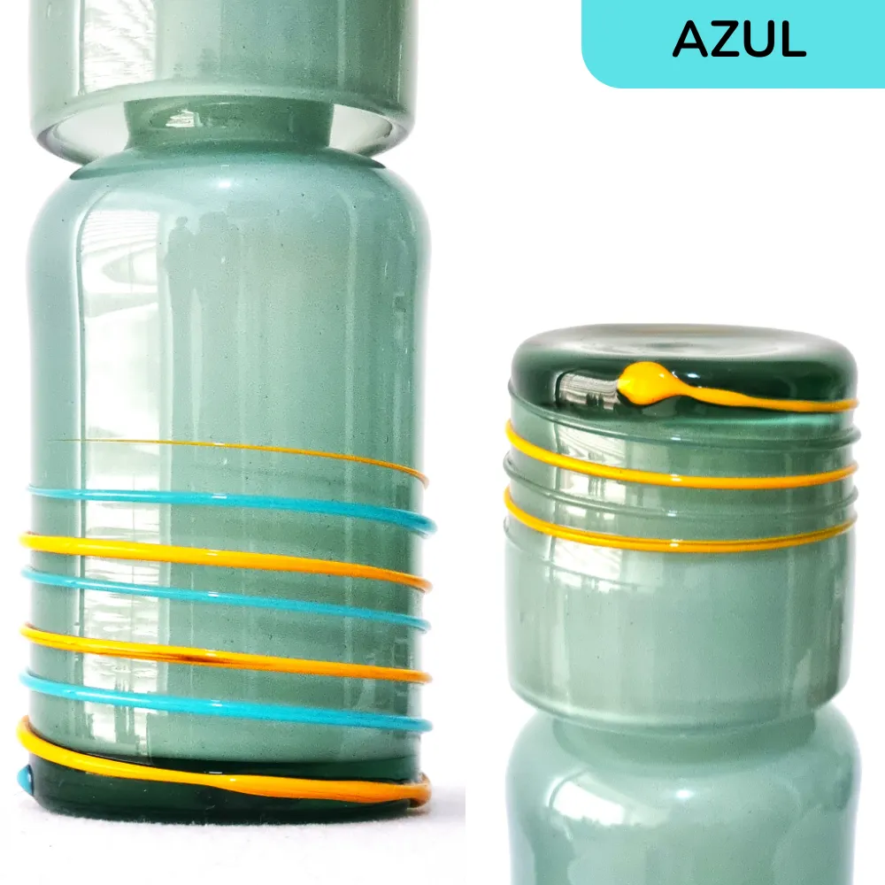 Detalle de cerca de la botella y vaso artesanal de vidrio azul con hilos decorativos de colores vibrantes.