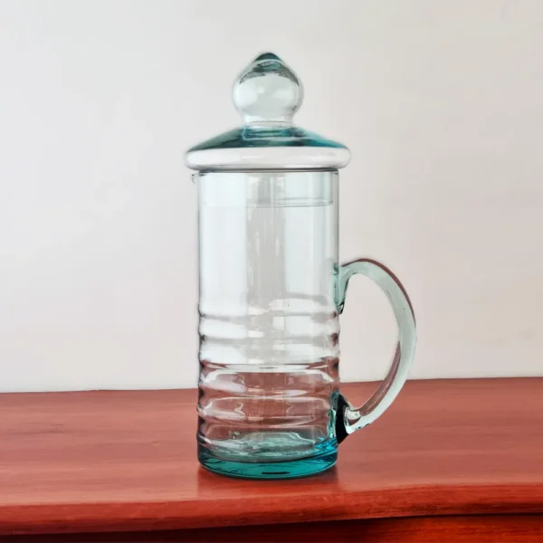 Jarra de vidrio para agua modelo Lemon de 1.2 litros, con su tapa, exhibida sobre una superficie de madera rojiza.