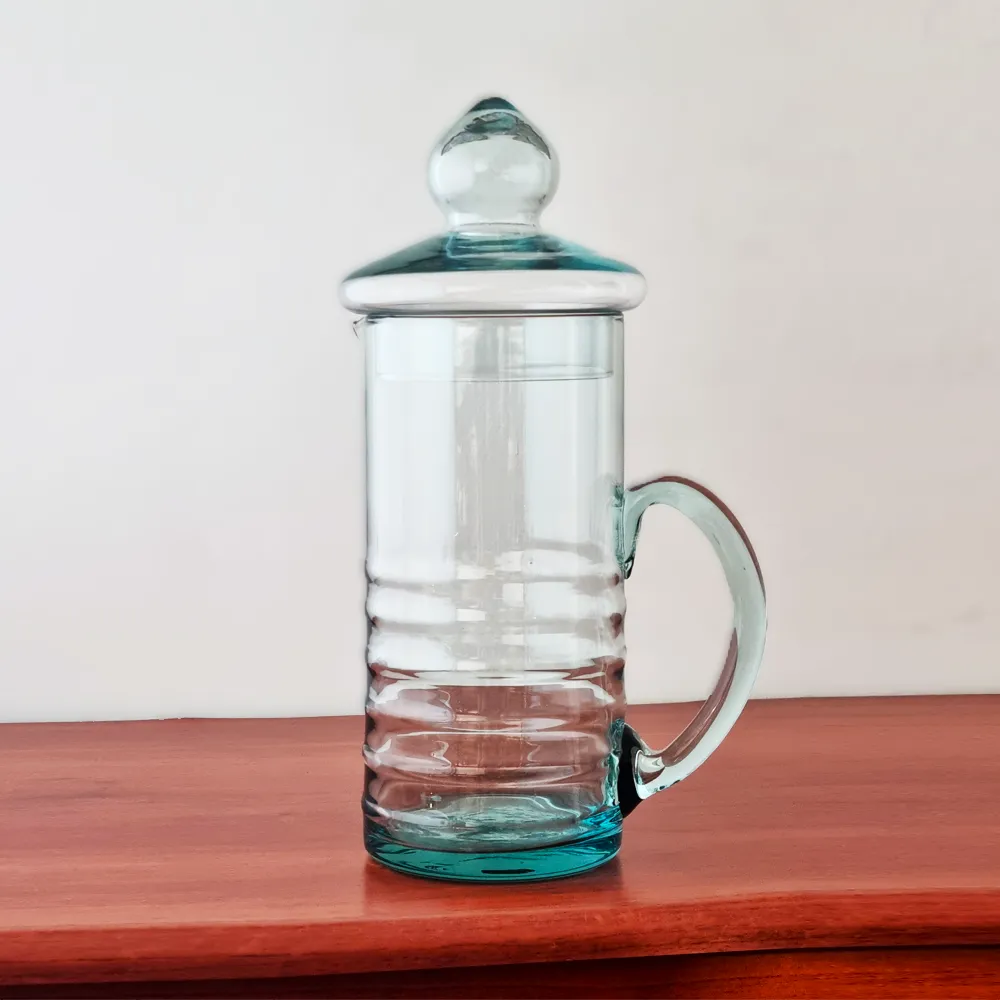 Jarra de vidrio para agua modelo Lemon de 1.2 litros, con su tapa, exhibida sobre una superficie de madera rojiza.